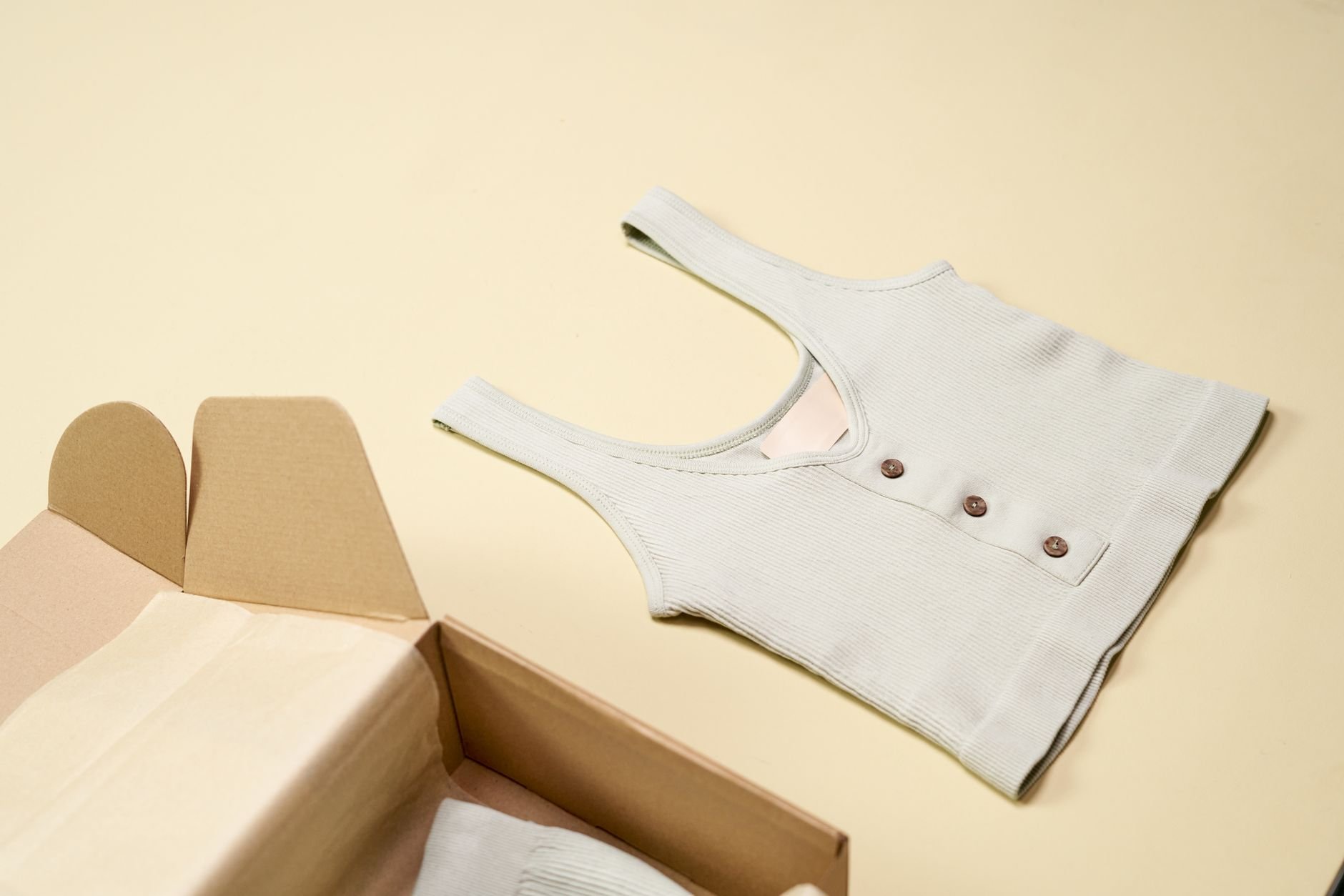A minimalist flatlay featuring a stylish sleeveless top next to an open cardboard box against a neutral background.